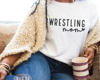 Może przedstawiać: Biała koszulka z napisem "WRESTLING mom" w kolorze czarnym z małym sercem po słowie "mom".