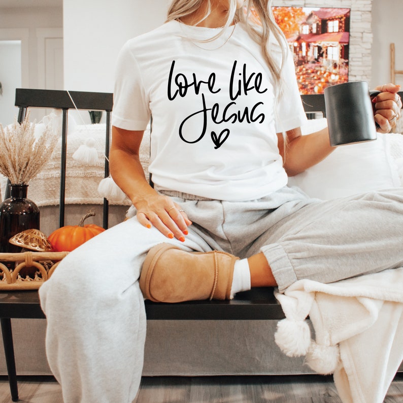 May include: A white t-shirt with the text "love like Jesus" in black script with a small heart below the text.