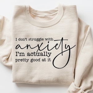 May include: A beige sweatshirt with the text "I don't struggle with anxiety I'm actually pretty good at it" printed in black.