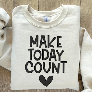 May include: A cream-colored sweatshirt with the text "MAKE TODAY COUNT" in black lettering and a black heart below the text.