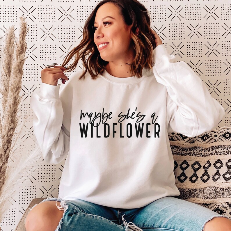 May include: White sweatshirt with black text that reads "maybe she's a wildflower".