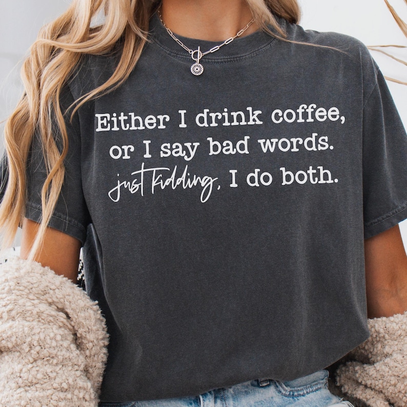 May include: Dark gray t-shirt with the text "Either I drink coffee, or I say bad words. just kidding, I do both." in white. The shirt has a casual, slightly worn look.