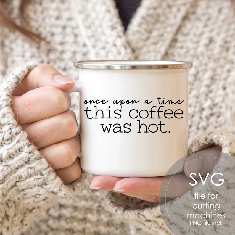 May include: White enamel mug with a black inscription that reads "once upon a time this coffee was hot." The mug is being held by a hand wearing a white sweater.