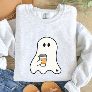 May include: A gray sweatshirt with a white ghost holding a coffee cup with a heart on the bottom. The ghost has two black eyes.