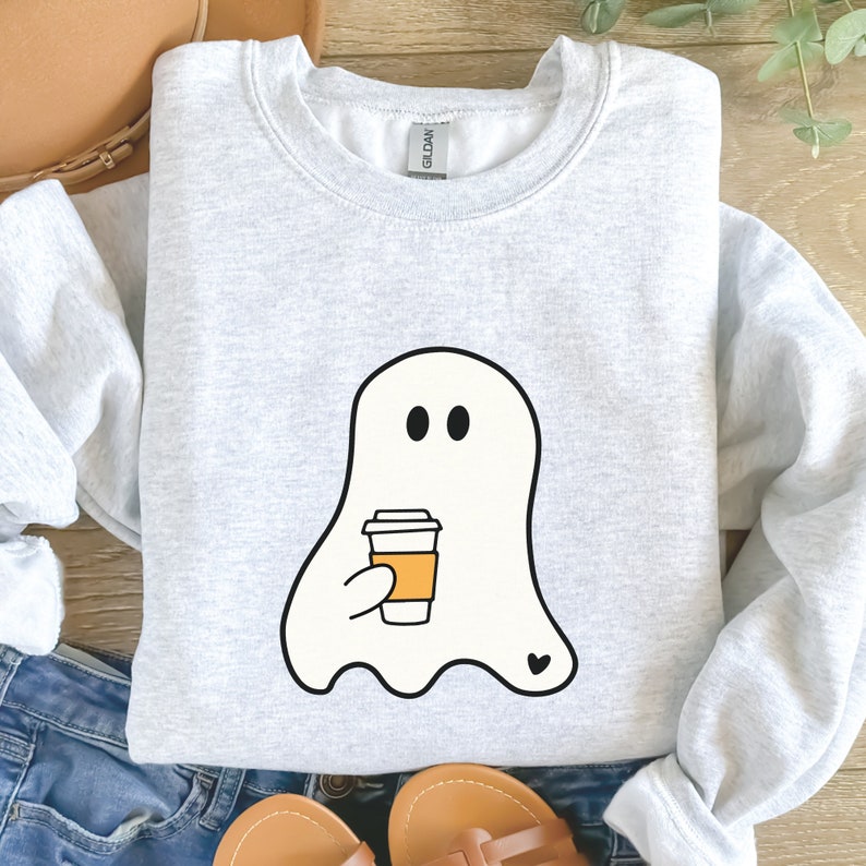 May include: A gray sweatshirt with a white ghost holding a coffee cup with a heart on the bottom. The ghost has two black eyes.