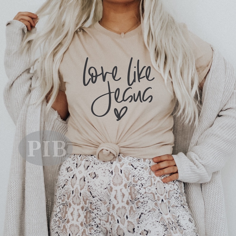 May include: A beige t-shirt with the text "Love like Jesus" in black script with a small heart below the text.