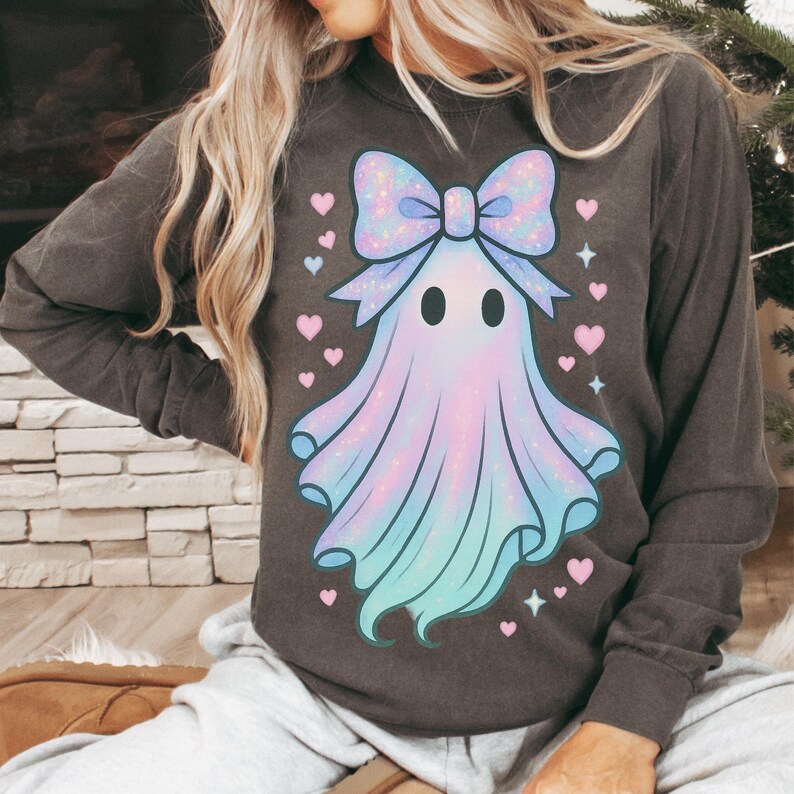 Puede incluir: Camiseta de manga larga gris oscuro con un dise&ntilde;o de fantasma pastel con un gran lazo, corazones y estrellas. El fantasma es una mezcla de tonos rosa, azul y morado. Un dise&ntilde;o caprichoso para Halloween o el uso diario.