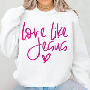 May include: White sweatshirt with a pink graphic that says "love like Jesus" with a pink heart.