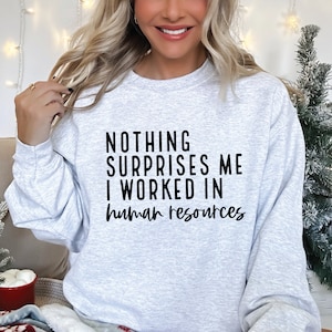 May include: A gray sweatshirt with the text "NOTHING SURPRISES ME I WORKED IN human resources" printed in black.