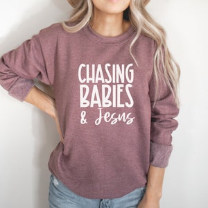 Może przedstawiać: Bordowy sweter z nadrukiem "CHASING BABIES & JESUS" w kolorze białym.