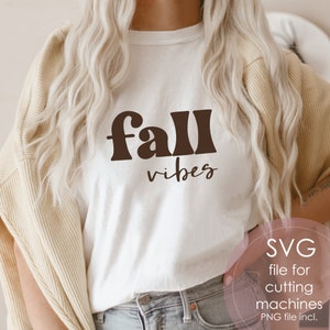 Może przedstawiać: Biała koszulka z napisem "fall vibes" w brązowych literach. Tekst jest w stylu retro. Koszulkę nosi osoba z długimi blond włosami. Obraz zawiera r&oacute;wnież tekst "SVG file for cutting machines PNG file incl."