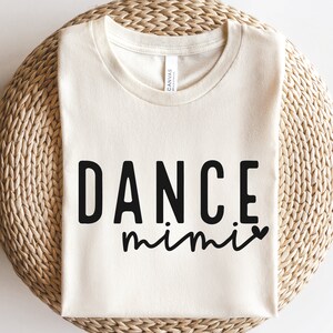 May include: A cream-colored t-shirt with the text "DANCE mimi" in black lettering. The text "mimi" is in a cursive font and includes a small heart.