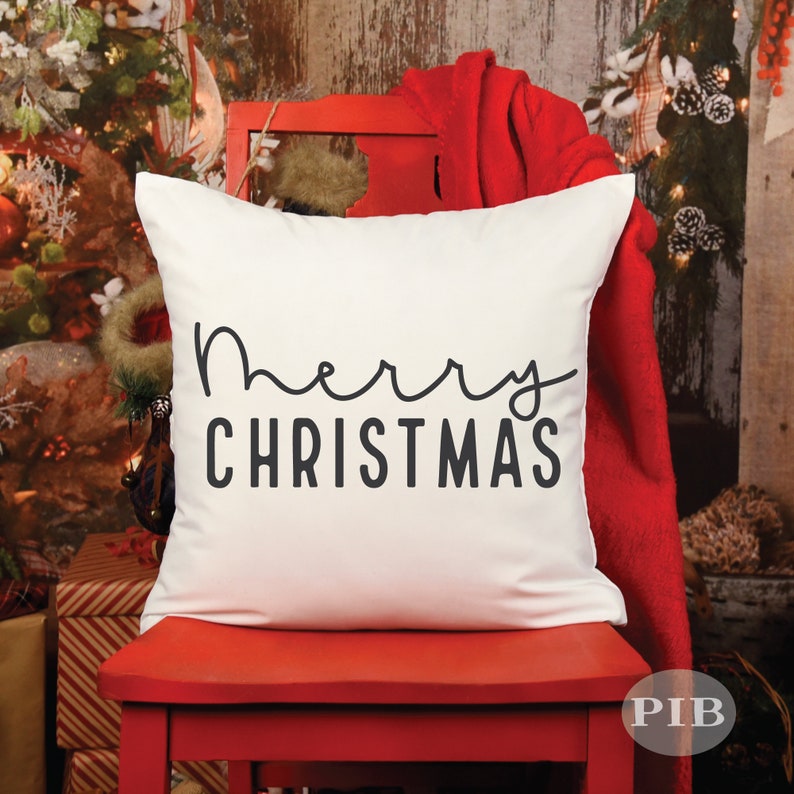 May include: White throw pillow with black text that reads "Merry Christmas" in a cursive font. The pillow is sitting on a red chair.
