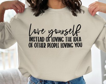 May include: A beige sweatshirt with the text "Love yourself instead of loving the idea of other people loving you" printed in black.
