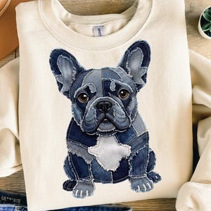 May include: A cream-coloured sweatshirt with a denim patchwork design of a French Bulldog. The dog is depicted in various shades of blue denim, with a white patch on its chest and brown eyes. The sweatshirt is a casual, comfortable style.