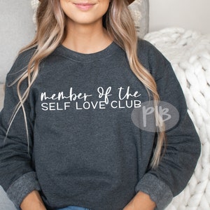 May include: A dark gray sweatshirt with the text "member of the SELF LOVE CLUB" printed in white on the front.