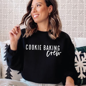 Puede incluir: Una sudadera negra con texto blanco que dice "Cookie Baking Crew".