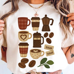 Puede incluir: Camiseta color crema con varias ilustraciones con temática de café. El diseño incluye tazas de café, vasos para llevar, una prensa francesa, granos de café y etiquetas de azúcar. Las ilustraciones son en tonos marrones y beige, con apariencia de tela cosida.