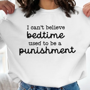 May include: White sweatshirt with the text "I can't believe bedtime used to be a punishment" printed on the front.