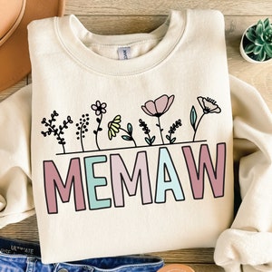 May include: A cream-colored sweatshirt with a graphic design of colorful flowers and the word "MEMAW" in pink, blue, and green letters.