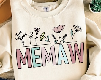 May include: A cream-coloured sweatshirt with a graphic design of colourful flowers and the word "MEMAW" in pink, blue and green letters.