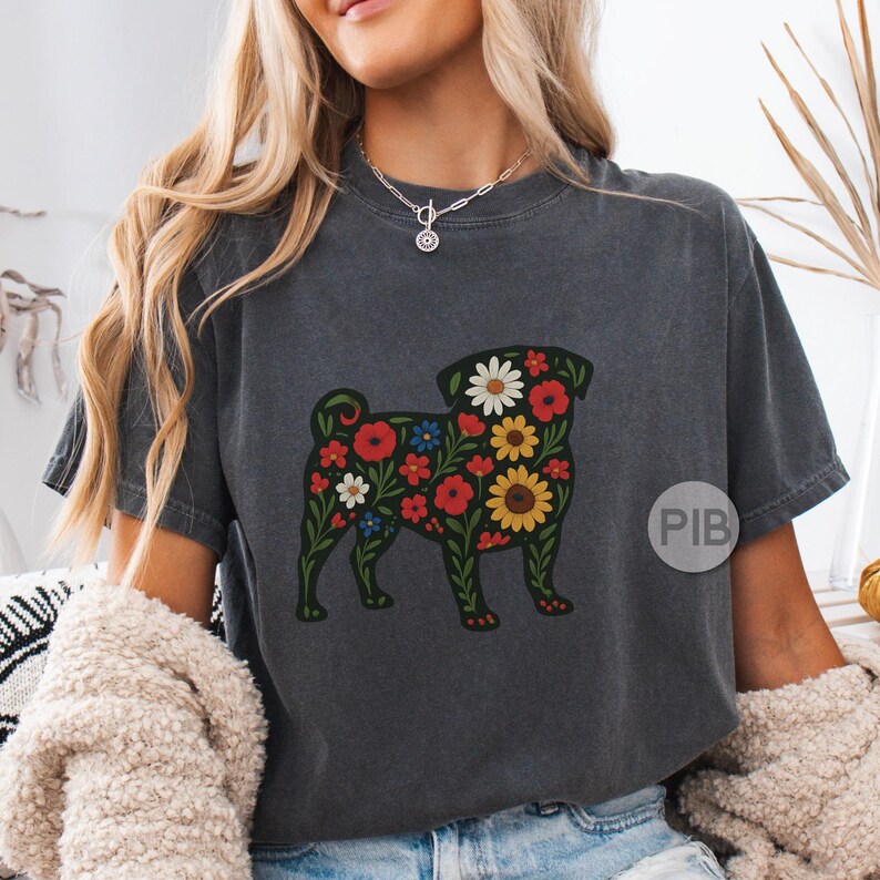 May include: Dark gray t-shirt featuring a floral pug design. The pug is outlined in green and filled with red, white, blue, and yellow flowers. The shirt has short sleeves and a crew neck.