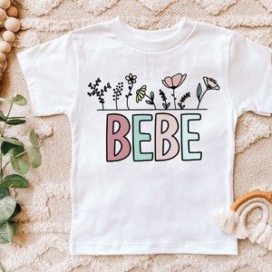 May include: White short-sleeved t-shirt with a floral design and the word "BEBE" in pink and green.