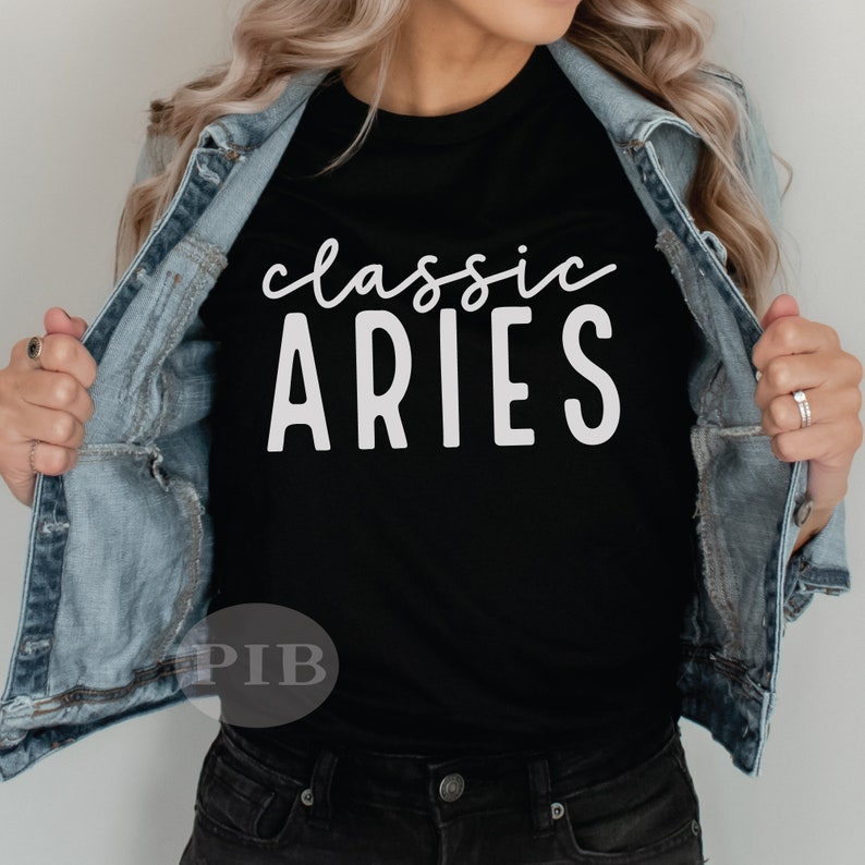 Puede incluir: Una camiseta negra con texto blanco que dice "classic ARIES". La camiseta la lleva puesta una persona con una chaqueta vaquera.