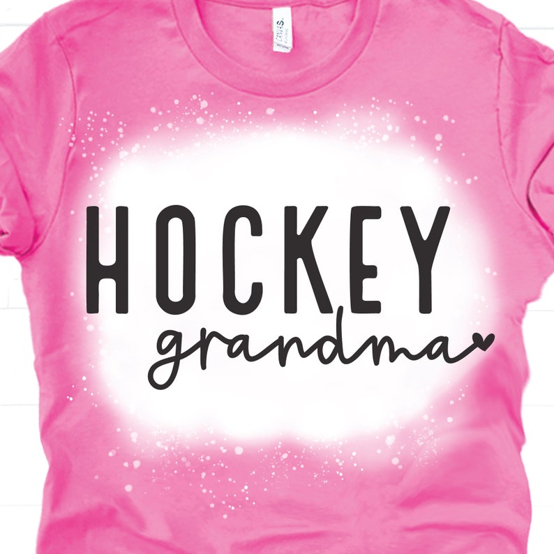 May include: Pink t-shirt with a white splatter design and the text "HOCKEY grandma" in black.