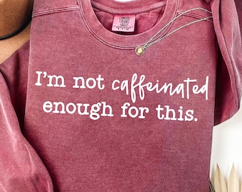 Könnte beinhalten: Ein weinrotes Sweatshirt mit dem weißen Text "I'm not caffeinated enough for this". Eine silberne Halskette mit einem kleinen Anhänger ist über die Vorderseite drapiert. Das Sweatshirt hat einen Rundhalsausschnitt und ein Comfort Colors-Etikett.