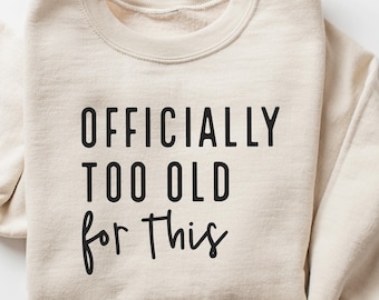 May include: A beige sweatshirt with the text "OFFICIALLY TOO OLD for this" printed in black.