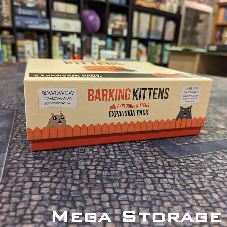 May include: A tan box with a red and orange bottom. The box has a picture of a cat on it and the text "Barking Kittens Exploding Kittens Expansion Pack".
