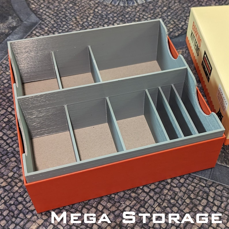 May include: A grey and orange storage box with the words "Barking Kittens" printed on the side. The box has multiple compartments for organising game pieces. The box is labelled "Mega Storage".