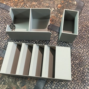 May include: Four gray plastic storage boxes with different sized compartments. The boxes are designed to hold small items like dice or game pieces.