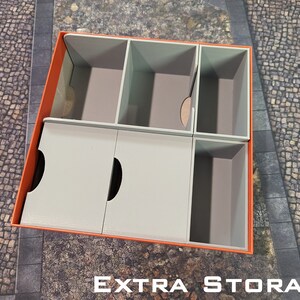 May include: An orange and grey cardboard box with dividers for organising small items. The box has the words "EXTRA STORAGE" printed on the bottom.