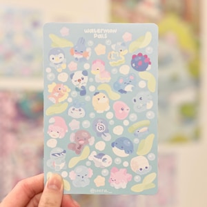 May include: A light blue sticker sheet with cartoon aquatic creatures and the text "Waterman Pals." The sheet has a light blue background with bubbles and leaf-shaped accents. The stickers are in various colours, including pink, blue, and yellow.