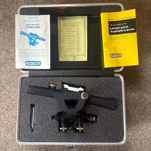 May include: A black Craftsman tilting level instrument with brass adjustment knobs and a plumb bob, housed in a foam-lined metal carrying case. Includes a parts list, a quality inspection checklist, and a yellow manual of instructions for the level.