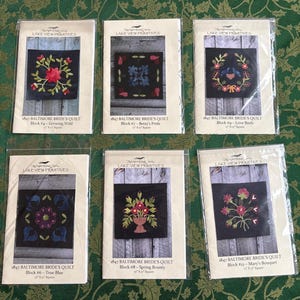 May include: Six quilt block patterns from Lake View Primitives. Each pattern features a different floral design in red, blue, and green on a black background. The patterns are labeled with the title "1847 Baltimore Bride's Quilt" and the block number.
