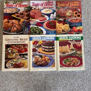 May include: A collection of cookbooks, including "Taste of Home" annual recipe books from 2000, 2001, and 2002, and "Ground Beef Cookbook" and "Quick Cooking" annual recipes. The covers feature images of various dishes.