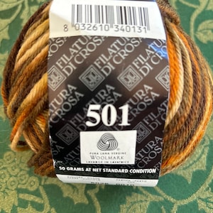 May include: A ball of brown, beige, and orange yarn with a label that reads "Filatura di Crosa" and "501". The label also includes the Woolmark logo and the text "Pura Lana Vergine" and "Lavabile in Lavatrice". The label states "50 grams at net standard condition".