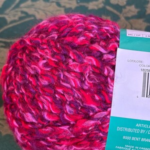 K&ouml;nnte beinhalten: Eine Kn&auml;uel pinkfarbenes, violettes und wei&szlig;es Garn mit einem Etikett, auf dem "LOT/LOTE: COLOR 18259" und "DISTRIBUTED BY/D 8000 BENT BRAM MADE IN CANADA FABRIQU&Eacute; AU CANADA HECHO EN CANADA SUPER BULKY" steht.