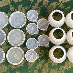 May include: A collection of white plastic lids and containers. The lids have a variety of designs, including a starburst pattern and a scalloped edge. The containers are round and have a smooth surface.