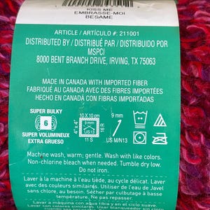 K&ouml;nnte beinhalten: Ein Kn&auml;uel super dickes Garn in den Farben Pink, Lila und Rot. Das Garn ist in Kanada aus importierten Fasern hergestellt und eignet sich zum Stricken oder H&auml;keln. Das Etikett enth&auml;lt Pflegehinweise, Gr&ouml;&szlig;eninformationen und die Artikelnummer 211001.