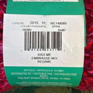 K&ouml;nnte beinhalten: Ein gr&uuml;nes und rotes Garnkn&auml;uel mit dem Text "Kiss Me, Embrasse-Moi, Besame" und den Produktinformationen "LOT/LOTE: 2015 10 WL148089 COLOR/COULEUR #: 01416 182591 85487 ARTICLE/ART&Iacute;CULO #: 211001 DISTRIBUTED BY / DISTRIBU&Eacute; PAR / DISTRIBUIDO POR MSPCI 8000 BENT BRANCH DRIVE, IRVING, TX 75063 MADE IN CANADA WITH IMPORTED FIBER FABRIQUE AU CANADA AVEC DES FIBRES IMPORT&Eacute;ES HECHO EN CANADA CON FIBRAS IMPORTADAS".