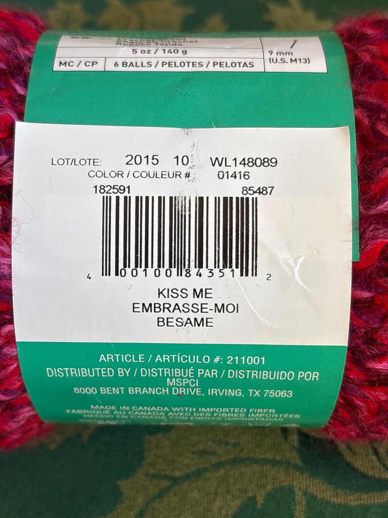 K&ouml;nnte beinhalten: Ein gr&uuml;nes und rotes Garnkn&auml;uel mit dem Text "Kiss Me, Embrasse-Moi, Besame" und den Produktinformationen "LOT/LOTE: 2015 10 WL148089 COLOR/COULEUR #: 01416 182591 85487 ARTICLE/ART&Iacute;CULO #: 211001 DISTRIBUTED BY / DISTRIBU&Eacute; PAR / DISTRIBUIDO POR MSPCI 8000 BENT BRANCH DRIVE, IRVING, TX 75063 MADE IN CANADA WITH IMPORTED FIBER FABRIQUE AU CANADA AVEC DES FIBRES IMPORT&Eacute;ES HECHO EN CANADA CON FIBRAS IMPORTADAS".