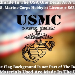 May include: Black USMC decal featuring the eagle, globe, and anchor emblem, with the text "USMC" and "Semper Fidelis." The decal is handmade in the USA. The background is a blurred American flag.