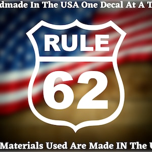 May include: White vinyl decal with a white shield shape and the text "RULE 62" inside. The decal is on a blurred background of an American flag.