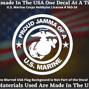 May include: A white decal with the U.S. Marine Corps emblem, encircled by the words "PROUD JAMMA OF A U.S. MARINE". The text "Handmade In The USA" and "All Materials Used Are Made In The USA" are also included. The background is blurred.