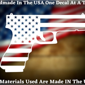 May include: White vinyl decal of a handgun with an American flag design. The decal is on a blurred background of an American flag.