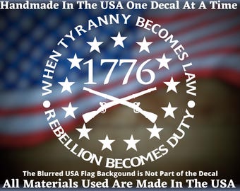May include: White vinyl decal with the text "When Tyranny Becomes Law Rebellion Becomes Duty" and "1776" with crossed rifles. The decal is on a blurred American flag background.